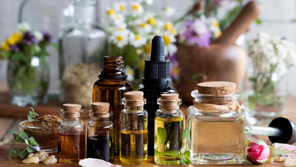 Assorted bottles of essential oils with herbs and flowers for aromatherapy on a wooden table