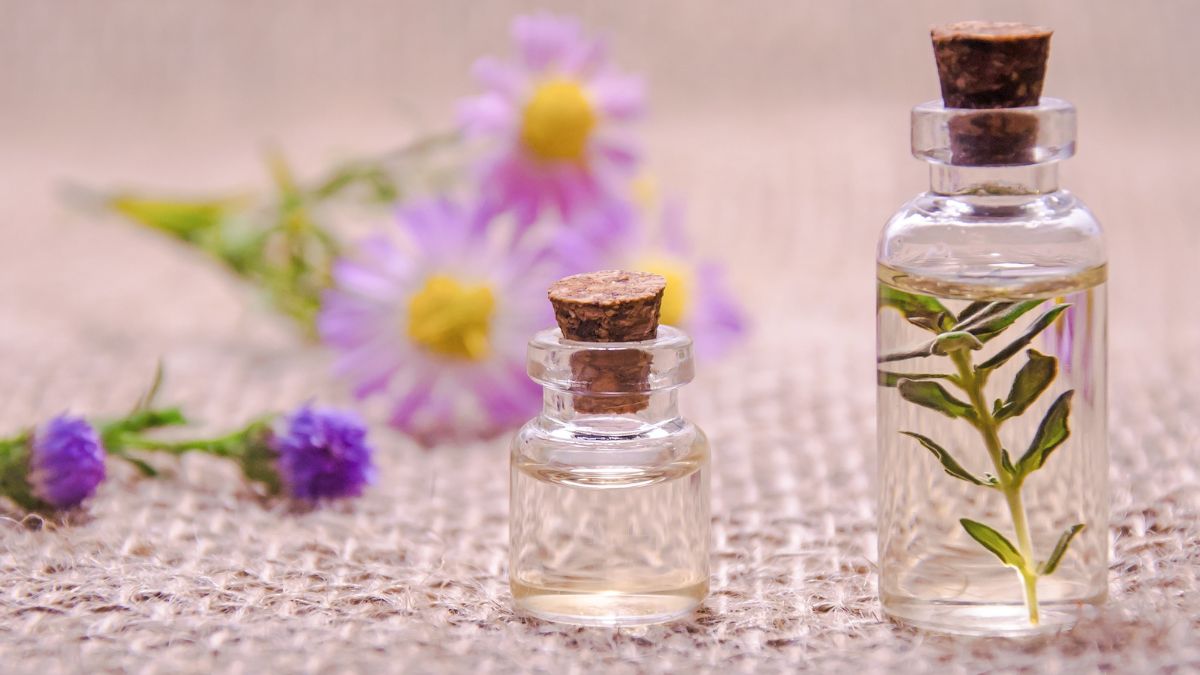 Lavender essential oil bottles on a table with flowers in the background, showing natural aromatherapy use.