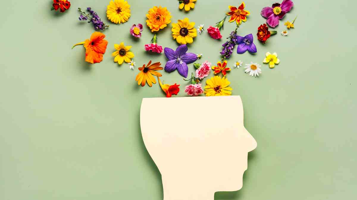 A flat illustration of a human head silhouette with colourful flowers spilling out from the top against a pale green background, symbolising Herbs for Mental Clarity and Focus.